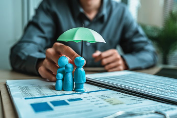 A wooden doll under an umbrella holding by agent represent life insurance and term insurance
