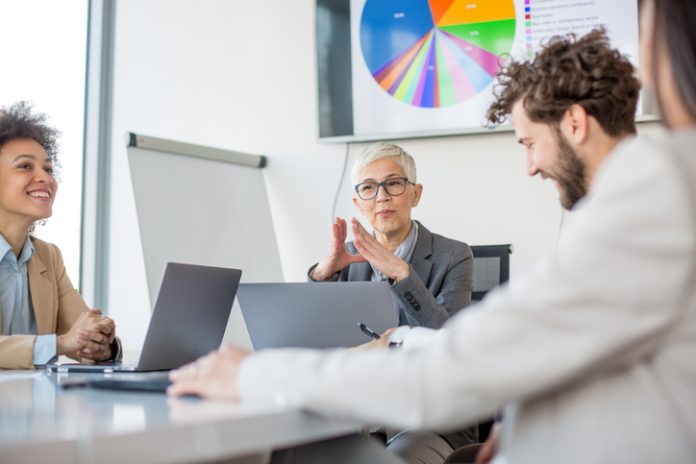 A group of business partners sit in a conference room and analyze the business of their corporations CEO using technology for presenting data
