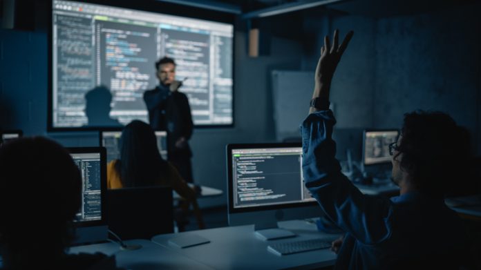 Teacher Giving Computer Science Lecture to Diverse Multiethnic Group of Female and Male Classmates in Dark College Room. Student Raises Hand and Answers Lecturer a Question About Software Engineering. Teacher Giving Computer Science Lecture to Diverse Multiethnic Group in Business Schools