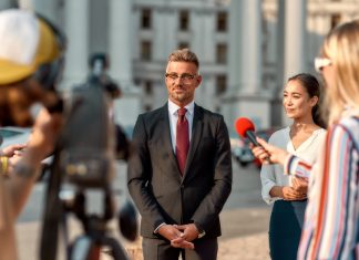 When Campaigns Hijack the Newsroom Horizontal shot of politician giving interview during campaign to journalists. People making interview using digital camera and equipment set at outdoor location.