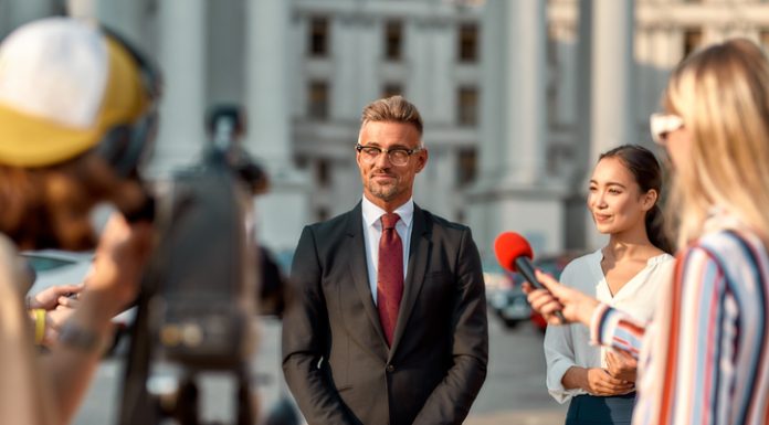 Horizontal shot of politician giving interview during campaign to journalists. People making interview using digital camera and equipment set at outdoor location.