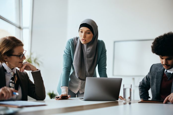 Young Muslim businesswoman using laptop while discussing with colleagues on a meeting in the office. Digital marketing company and SEO team in Dubai