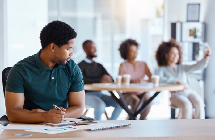 Reject, sad and antisocial professional employee sitting at his desk as outcast in the workplace. Workplace Microaggressions concept