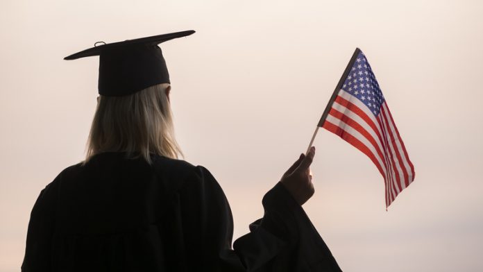 Rear view of graduate woman with usa flag in hand Minimum GPA for MS in US Universities