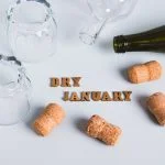 Overturned glasses, empty bottles, corks and text dry january on gray background