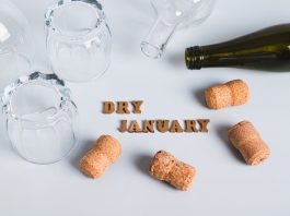 Overturned glasses, empty bottles, corks and text dry january on gray background