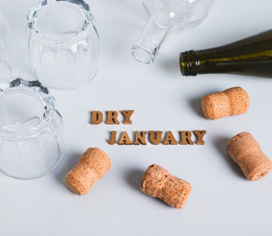 Overturned glasses, empty bottles, corks and text dry january on gray background