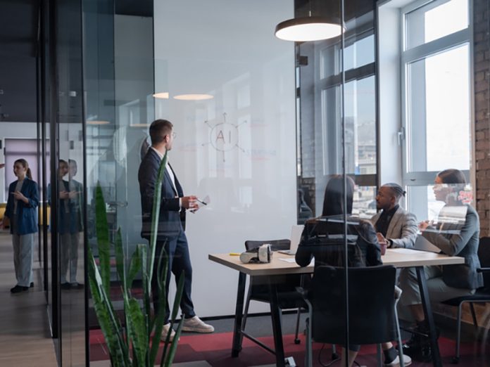 Modern office meeting with diverse professionals discussing artificial intelligence strategy. Concept of teamwork, technology, and corporate innovation in a contemporary workspace From Compliance to Conviction: Leadership Readiness as the Binding Constraint of the AI Era