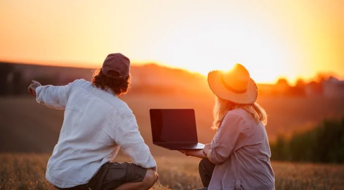 Farmers using laptop for smart farming analysis while observing rural field during sunset. Concept of modern agriculture and farm innovation