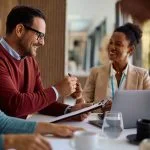 Happy couple coming to and agreement with their financial advisor. Focus is on man signing a contract following the Fiduciary Standard