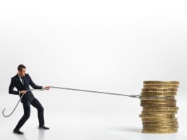 Businessman pulling stack of big golden coins with a rope isolated on white background. Making money. Profit and advantage. Earning a fortune.
