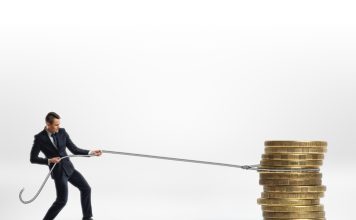 Businessman pulling stack of big golden coins with a rope isolated on white background. Making money. Profit and advantage. Earning a fortune.