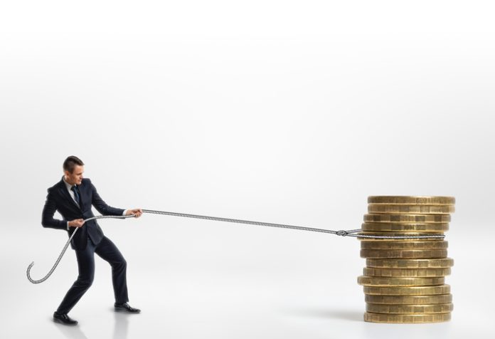 Businessman pulling stack of big golden coins with a rope isolated on white background. Making money. Profit and advantage. Earning a fortune.