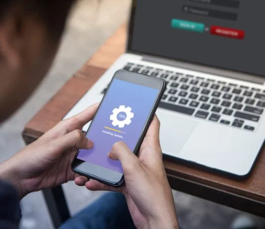 While working on laptop businessman installing OTA firmware update his smartphone at outdoor cafe