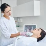 Experienced female dermatologist using a Ultherapy Prime beauty device for tightening the skin on her patient neck