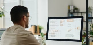 Key Features of SAP SuccessFactors for HR Teams Young HR manager looking through statistic data on computer screen and typing on keyboard while sitting by desk in openspace offic using SAP SuccessFactors software.