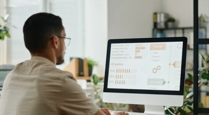 Young HR manager looking through statistic data on computer screen and typing on keyboard while sitting by desk in openspace offic using SAP SuccessFactors software.