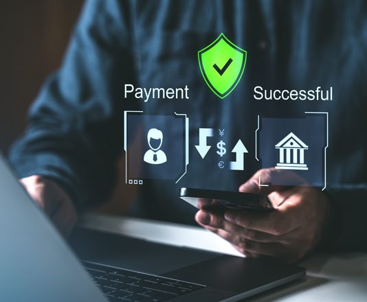 A person using a smartphone and laptop with holographic payment icons, secure shield, and success symbols. Concept of secure online payment