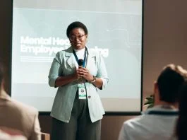 Seminar, speaker and woman with mic, talking and public speaking for mental health in workplace or stage. Business, presentation and employee with speech for audience, people and podium for presenter