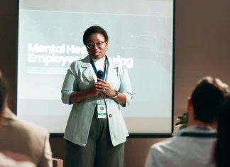 Seminar, speaker and woman with mic, talking and public speaking for mental health in workplace or stage. Business, presentation and employee with speech for audience, people and podium for presenter