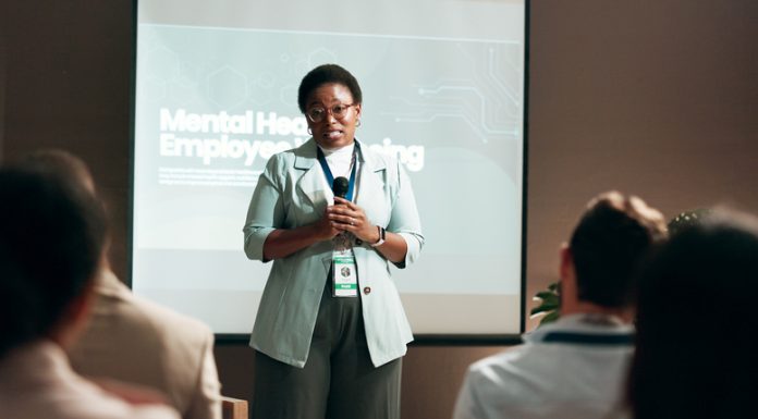 Seminar, speaker and woman with mic, talking and public speaking for mental health in workplace or stage. Business, presentation and employee with speech for audience, people and podium for presenter