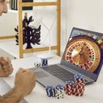 Happy, excited man sitting at table with poker chips and looking at casino wheel on screen on GameZone Casino app