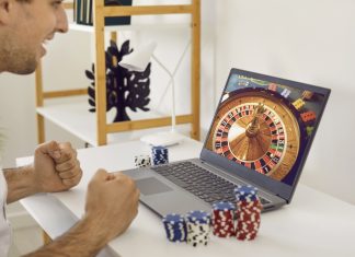 Happy, excited man sitting at table with poker chips and looking at casino wheel on screen on GameZone Casino app