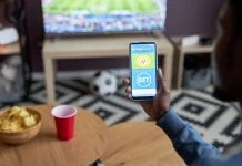 Close up of male hand holding smartphone with online sports bets on screen while watching football match at home,