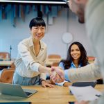 Diverse businesswomen greeting new team member with a handshake in a modern office, celebrating collaboration for Talent Strategy
