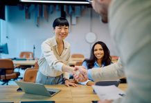 Diverse businesswomen greeting new team member with a handshake in a modern office, celebrating collaboration for Talent Strategy