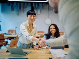 Diverse businesswomen greeting new team member with a handshake in a modern office, celebrating collaboration for Talent Strategy