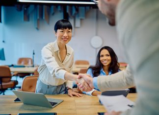 Diverse businesswomen greeting new team member with a handshake in a modern office, celebrating collaboration for Talent Strategy