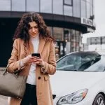 Car Insurance Explained: Why Third-Party Car Insurance Online is Mandatory Young woman using phone and standing by the car for car insurance
