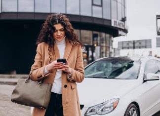 Young woman using phone and standing by the car for car insurance