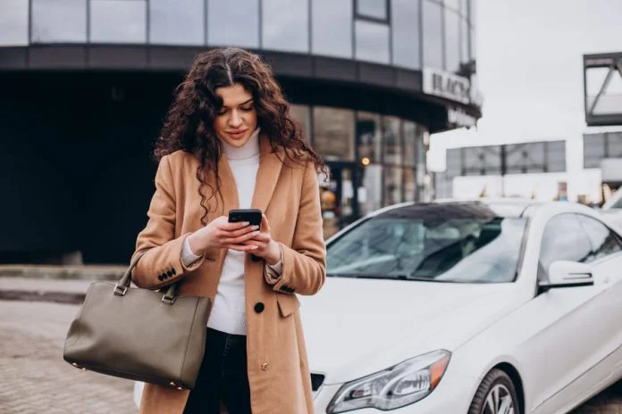 Young woman using phone and standing by the car for car insurance
