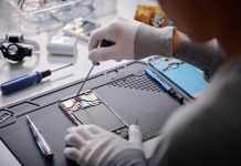 Over shoulder shot of unrecognizable technician repairing disassembled smartphone, circuit with screwdriver