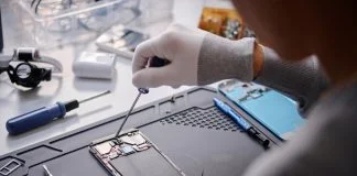 Over shoulder shot of unrecognizable technician repairing disassembled smartphone, circuit with screwdriver