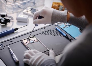 Over shoulder shot of unrecognizable technician repairing disassembled smartphone, circuit with screwdriver