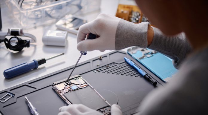 Over shoulder shot of unrecognizable technician repairing disassembled smartphone, circuit with screwdriver