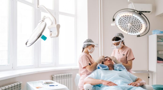 Professional trichologist surgeons carry out hair FUE Sapphire method hair transplant surgery in operating room to male patient with hair loss problem.