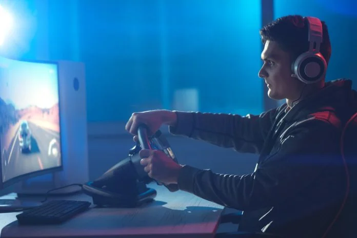 The guy gamer with headphones playing video game on his personal computer The guy gamer with headphones playing racing game on his personal computer