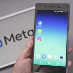 Mobile display with logo of Facebook, WhatsApp and Instagram apps in against blurred META logotype
