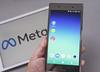 Mobile display with logo of Facebook, WhatsApp and Instagram apps in against blurred META logotype