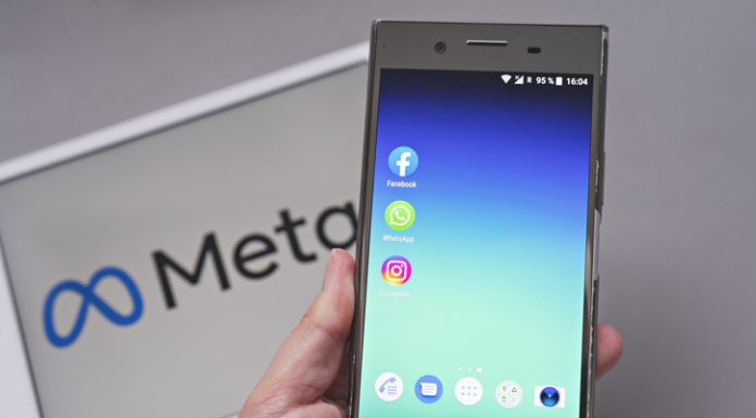 Mobile display with logo of Facebook, WhatsApp and Instagram apps in against blurred META logotype