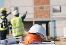 Structural engineer and architect working with blueprints discuss at the outdoors construction site.
