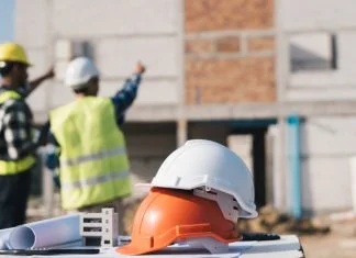 Structural engineer and architect working with blueprints discuss at the outdoors construction site.
