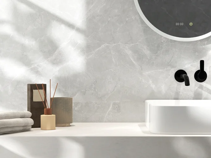 Reed stick diffuser, aroma oil, towel on cream stone vanity counter top in sunlight on white marble wall, wash basin bathroom tile design
