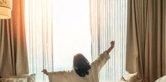 Asian woman waking up from good sleep on bed in weekend morning resting in comfort bedroom looking toward city view, having happy, productivity, work-life quality balance lifestyle