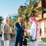 Business Setup in Saudi Arabia: The Complete Guide for Foreign Investors Mature Arabic businessman shaking hands with Caucasian partners in Jeddah Culture, Saudi Arabia Square featuring traditional architecture and palm trees.