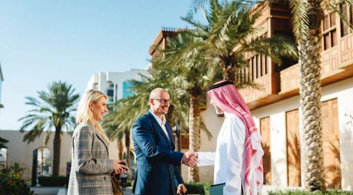 Business Setup in Saudi Arabia: The Complete Guide for Foreign Investors Mature Arabic businessman shaking hands with Caucasian partners in Jeddah Culture, Saudi Arabia Square featuring traditional architecture and palm trees.